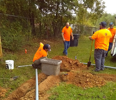 Four men in orange T-shirts digging the earth